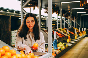 Young beautiful dark-haired woman holds oranges in market. Seller of organic fruits at local...