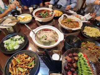A feast featuring chicken soup, stir-fried dishes, vegetables, fruits, and various Chinese-style...