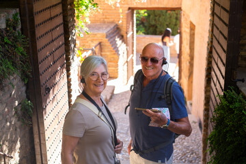 Happy senior couple of travelers visiting Granada listening to information via audio guide. Elderly man and woman enjoying travel, vacation and retirement in Europe