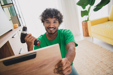 Portrait of nice young man hold drill fix repair furniture wear t-shirt modern green interior flat...