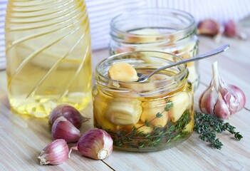Spoon with garlic clove pickled in sunflower oil and thyme.  A glass jar full of garlic cloves...
