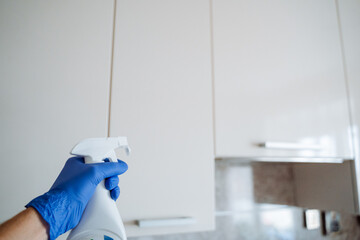 In a clean kitchen, a person in electric blue gloves shows safe ways to use a spray bottle,...