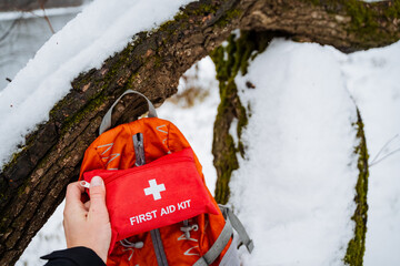 A person is standing in the snow, holding a first aid kit in one hand, and next to them, there is a...