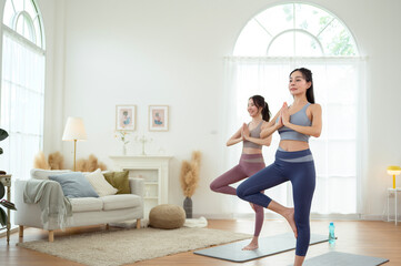 Fototapeta premium Two young Asian woman friends practicing yoga at home.