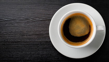 A coffee cup on a saucer viewed from above, placed to the side on a dark wooden table with copy space for text