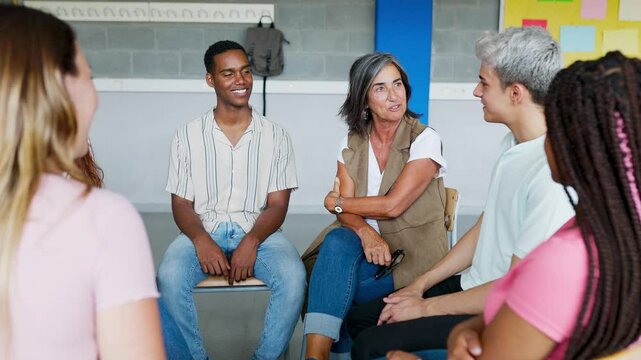 Young group of teenage students discussing in classroom sitting in circle with female teacher, giving an opinion on a debate topic. Education concept