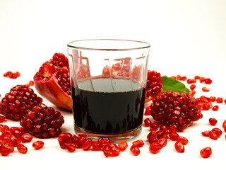 Freshly squeezed pomegranate juice in a glass. Slices and seeds of ripe pomegranate lie on a white table.