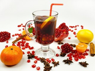 A glass cup of mulled wine with  a drinking straw  and ingredients for its preparation are on a white table