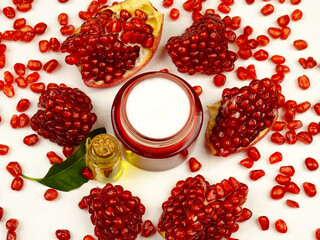 Bottle with pomegranate oil, jar with cream based on it and slices of fresh pomegranate on white background, top view. Natural cosmetics for face and body.