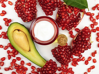 Bottle with extract oil, jar with cream based on pomegranate and avocado, slices of these fresh fruits are on white background, top view 