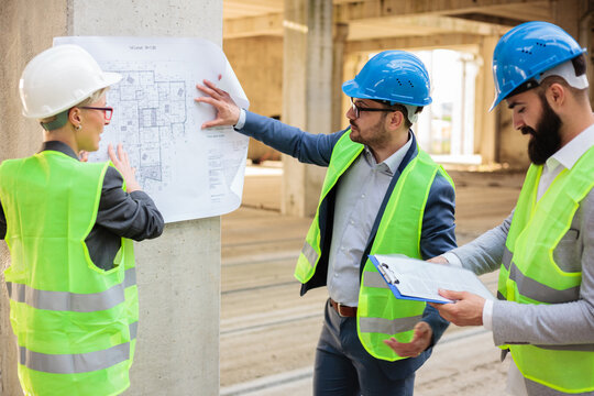 Team of successful young architects and business partners during a meeting on a construction site. Looking at architectural drawings and blueprints.