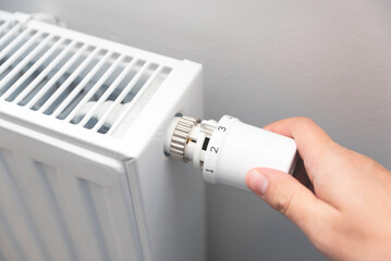 Modern white radiator, hand holding thermostat