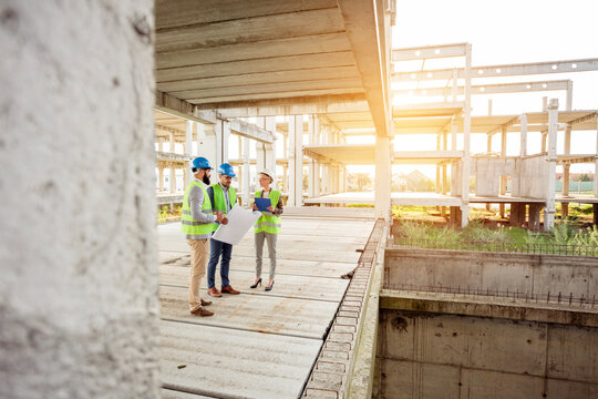 Team of successful young engineers and business partners inspecting works on a construction site. Wide angle view.
