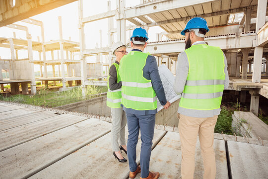 Team of successful young engineers and business partners inspecting works on a construction site. Wide angle view.
