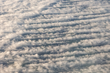 Windmills, wind turbines above the fog clouds creating vortex trails