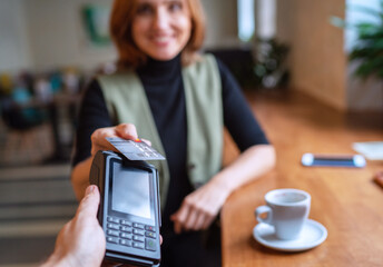 Young woman holding credit doing wireless bank payment with POS terminal process acquire at table...
