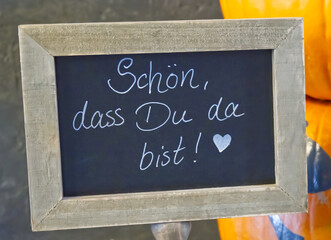Auf einer Schiefer Tafel mit Holzrahmen steht !Schön, dass Du da bist ! mit einem Herz dahinter.