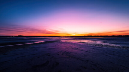 Vibrant sunset over a tranquil beach with dark sand and a clear sky transitioning from pink to deep blue hues.
