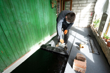 A man uses a kerosene lamp to heat a roll of bitumen for waterproofing the floor.