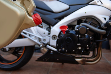 A can of motor oil for a motorcycle. Gold colour with a red cap. A motorcycle in the background. Maintenance concept.