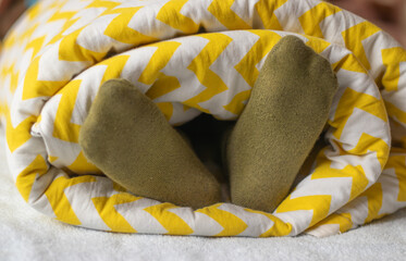 The child's feet in socks stick out from under the blanket. Daytime or morning sleep. Colored blanket.  Happy childhood concept.