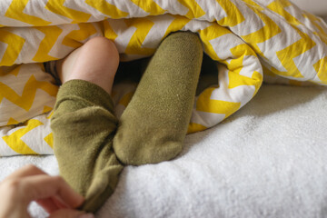 The child's feet in socks stick out from under the blanket. Daytime or morning sleep. Colored blanket.  Happy childhood concept.