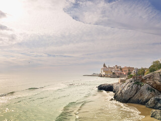Beautiful ocean view with gentle waves breaking on the shore, a distant village and misty mountains. A quiet and peaceful landscape, perfect for relaxing and enjoying the tranquility.