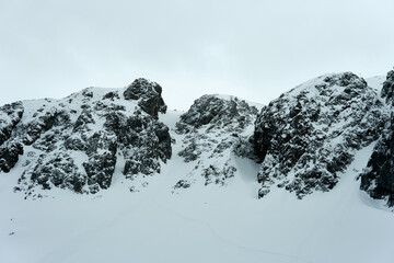 Snow-covered peaks rise dramatically against a cloudy sky in a remote mountainous region during...