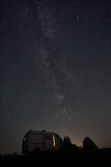 Fototapeta premium Starry night sky over camper van parked in a remote area with the Milky Way visible
