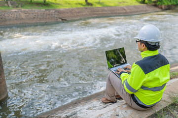 A engineering doing his checking routine. He is wearing hard hat and engineer uniform.Standing by the rail by the dam.Monitor water levels from the heavy rain that has been falling for several days.