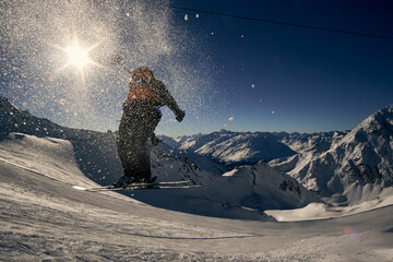 Snowboarder performs a jump in the mountains under bright sunlight with stunning snowy peaks in the...