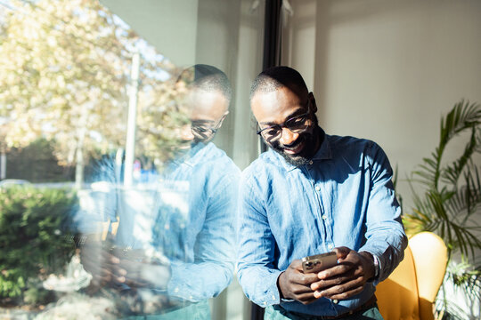 Smiling black businessman using smartphone near office window