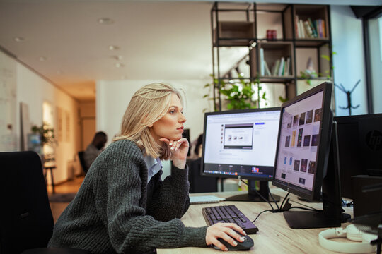 Focused woman working at dual monitors in modern office setting