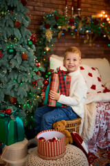 Cute boy hugging a gift box next to Christmas tree. A child in anticipation of miracles and a holiday