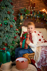 Cute boy hugging a gift box next to Christmas tree. A child in anticipation of miracles and a holiday