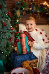 Cute boy hugging a gift box next to Christmas tree. A child in anticipation of miracles and a holiday