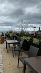Empty outdoor cafe with modern wicker chairs and tables on a sandy patio. Decorative planters...