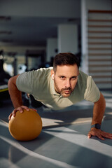 Male athlete doing one arm medicine ball push-up during cross training in  gym