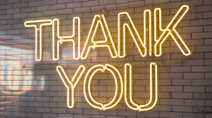 A bright yellow neon sign displays the words 'Thank You' against a textured brick wall, creating a warm and inviting atmosphere.