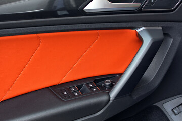Fototapeta premium Orange interior of sports crossover. Car leather Orange interior details of door handle with windows controls and adjustments. Modern car orange leather interior. Sports car interior.