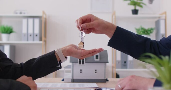 Business man in the office gives the keys to the house to a woman, hands close-up. Concept of buying real estate, mortgage. Investment in a new building, house rental, real estate agency, slowmotion