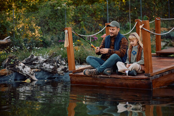 Happy father and daughter fishing by  lake in autumn.