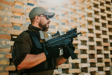 Soldier holding modern assault rifle and wearing tactical gear near brick wall