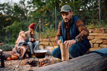 Mid adult man chopping firewood while camping with his family in autumn.