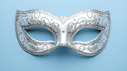 Bright, glittering silver New Year's masquerade mask with intricate patterns, isolated on a soft blue background