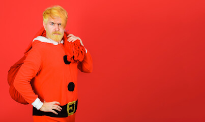 Bearded man in Santa Claus costume carrying big sack with Christmas gifts for kids. Christmas or New Year holidays. Serious Santa man with sack bag with Christmas presents. Gift delivery. Copy space.