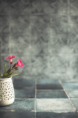 A decorative vase with flowers sits on a dark, textured tiled surface against a blurred gray background.