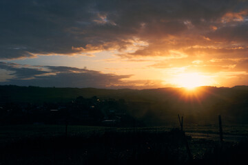 Naklejka premium Sunrise over rolling hills creating a golden glow in a quiet countryside landscape