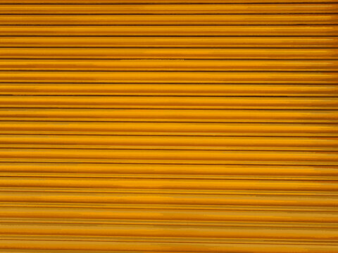 Abstract orange rolling corrugated metal pattern. Background metal corrugated texture in orange brown. Yellow shutter for compositions. Orange metallic texture detailed and seamless wall, grunge.