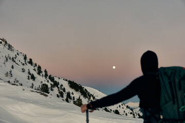 Hiker enjoying a peaceful winter evening under the full moon in a snowy mountain landscape